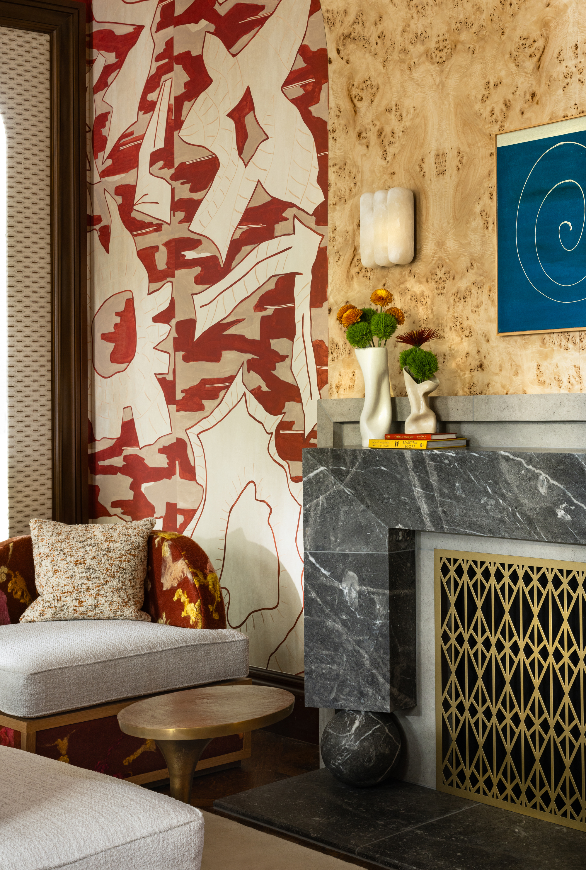 A corner of a living room with a marble fireplace, burl wood veneer, and a dramatic abstract wallpaper