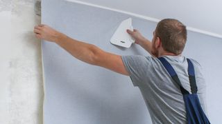 Man hanging wallpaper on wall