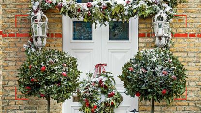 House exterior with Christmas garland and matching bay trees either side of the door to show the Curtain pole Christmas decoration trend