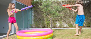 Image of two kids playing with water guns by an inflatable pool