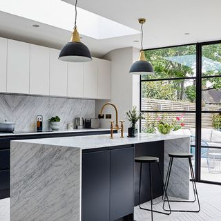 A kitchen with white wall and grey base units with a kitchen island with marble waterfall countertop