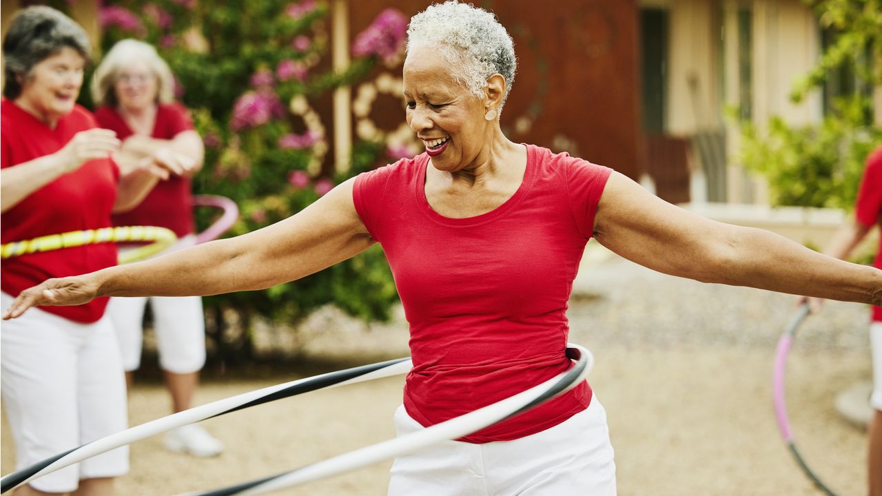 An older woman plays with a hula hoop with a group of other women.