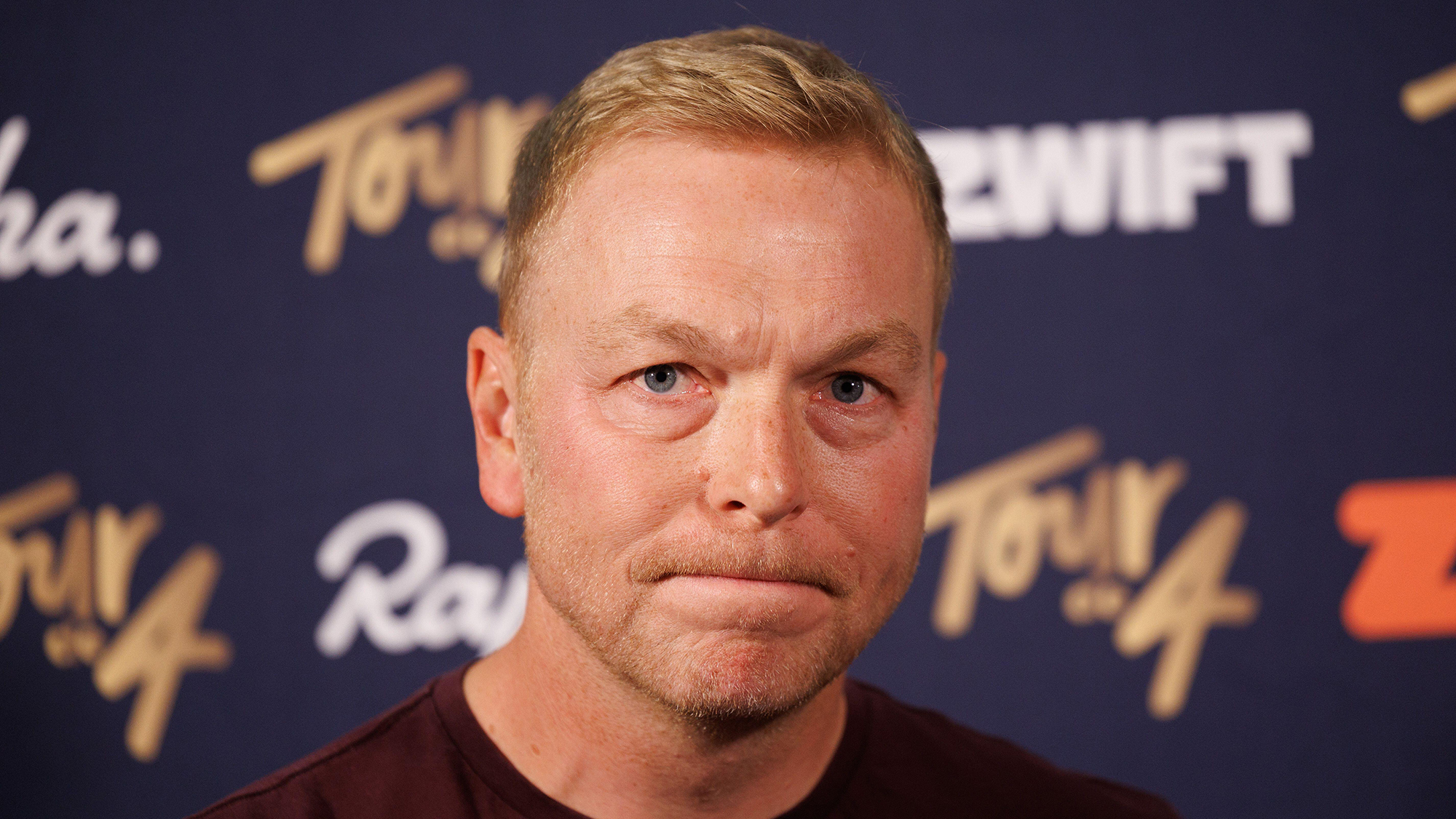 Portrait image of Chris Hoy in front of a black backdrop bearing Zwift and Rapha logos