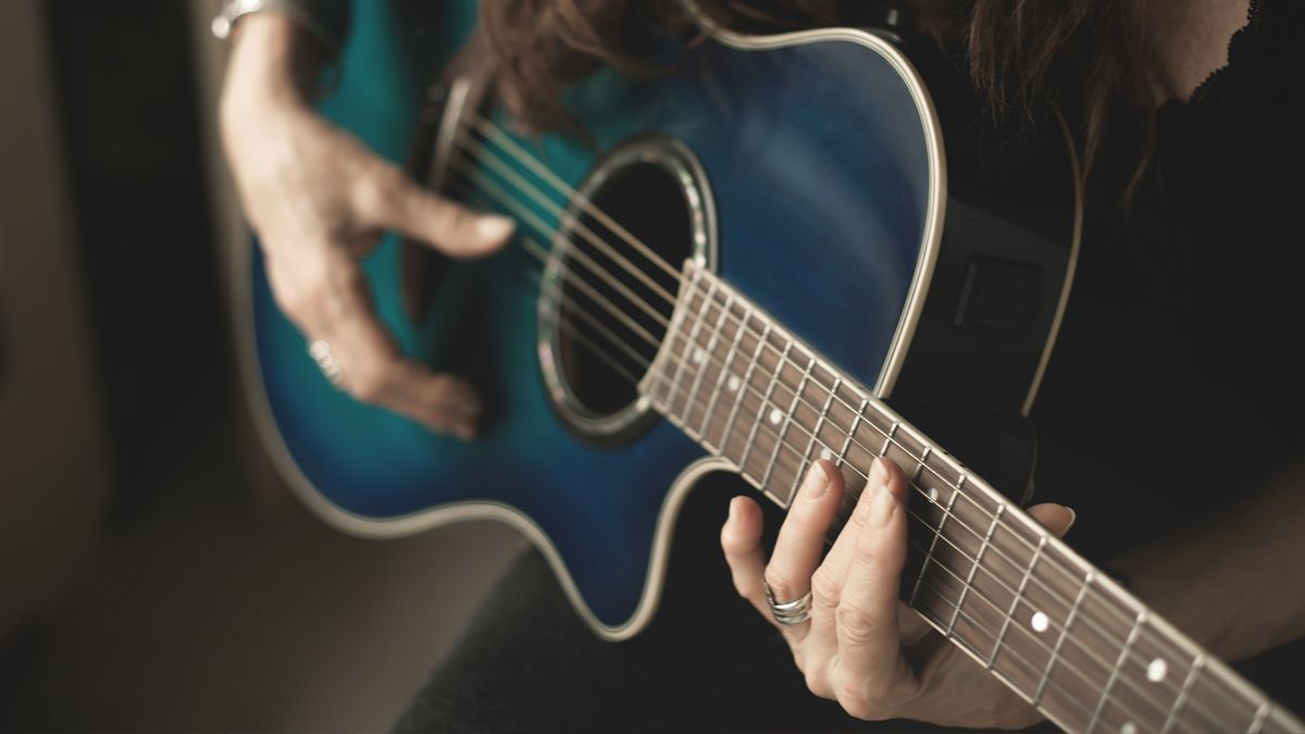 A guitarist plays an ocean blue acoustic guitar