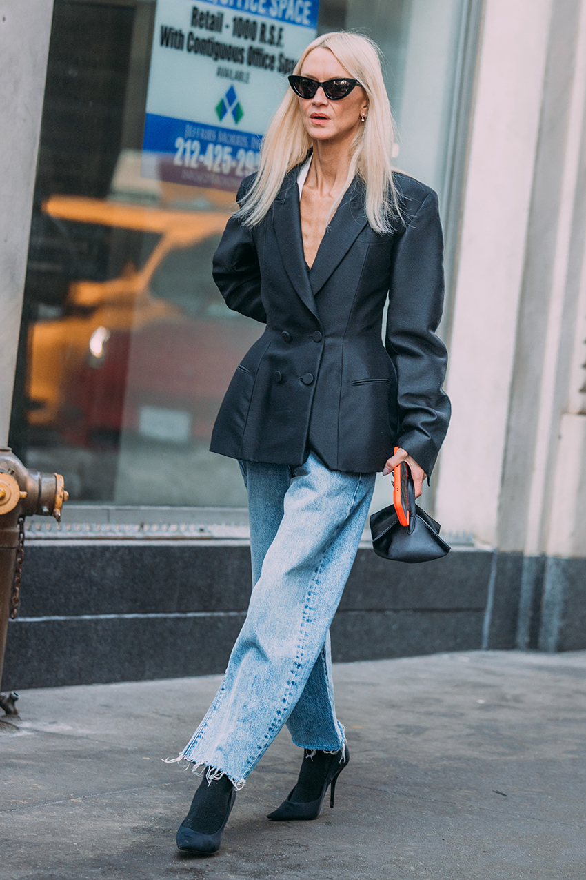 A woman wearing a black blazer, blue jeans, and black heels