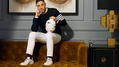 Jonathan Adler sat on the back of a sofa holding a vase