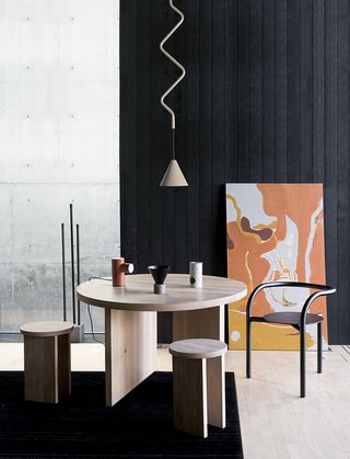 Wooden table and stools, black chair, small sculptures on table and painting in the background