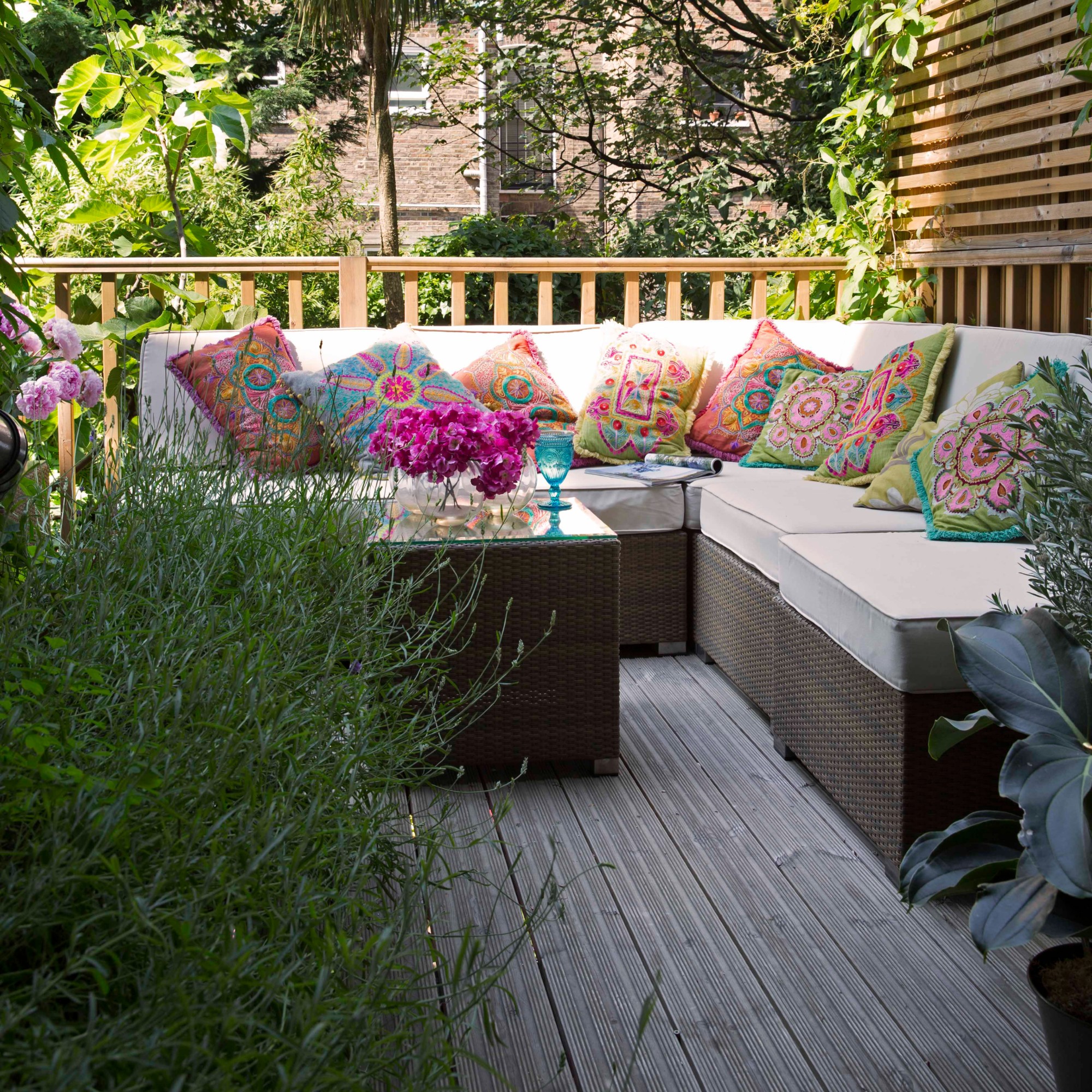A balcony with a corner modular sofa in a rattan effect decorated with colourful patterned outdoor cushions