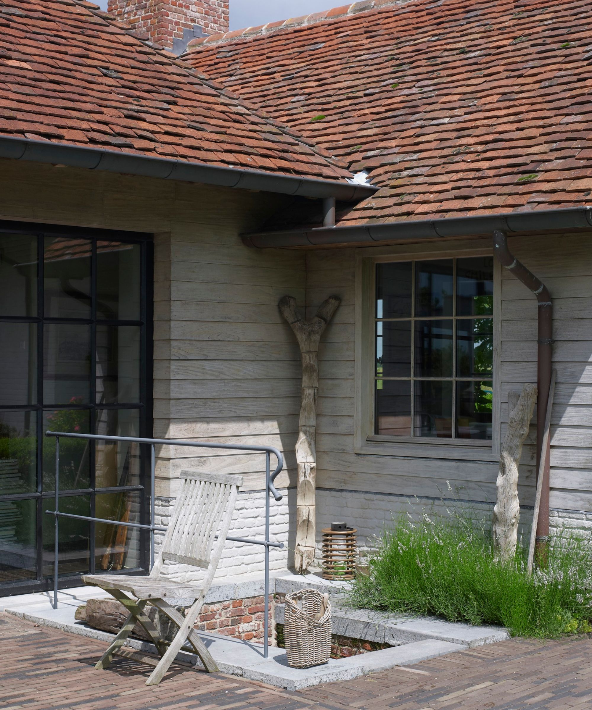 A wood panelled home with crittal windows, red roof tiles, a wooden chair, and a gutter and drain pipe seen.