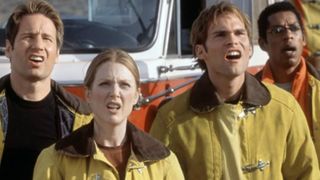 Screenshot from the movie Evolution. A team of four people are all looking up in disbelief. Each team member is wearing a yellow firefighter suit to protect themselves. There is a fire engine in the background.