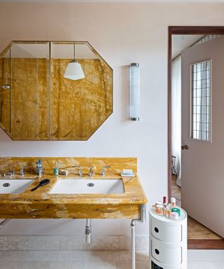 neutral bathroom with ochre toned marble washstand and backsplash and art deco style mirror