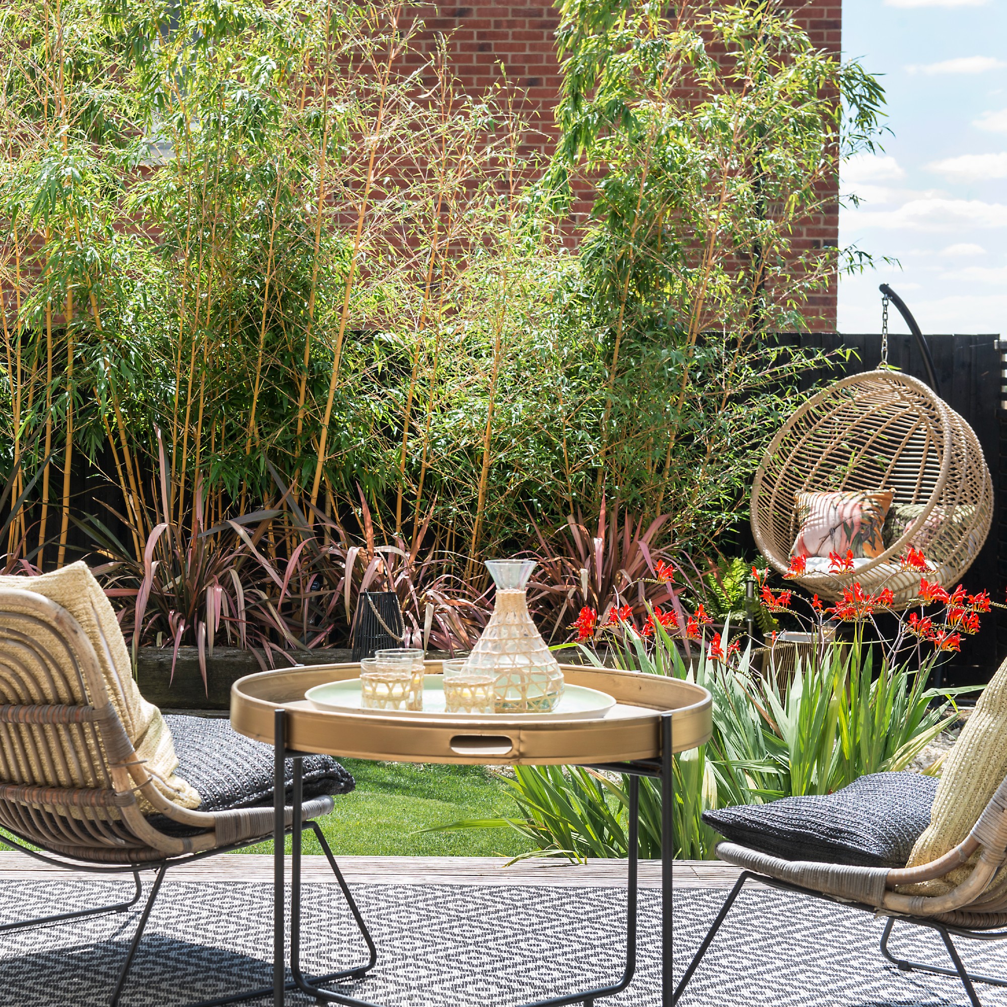 A garden with a rattan garden chair set and a coordinating coffee table and an egg chair in the background