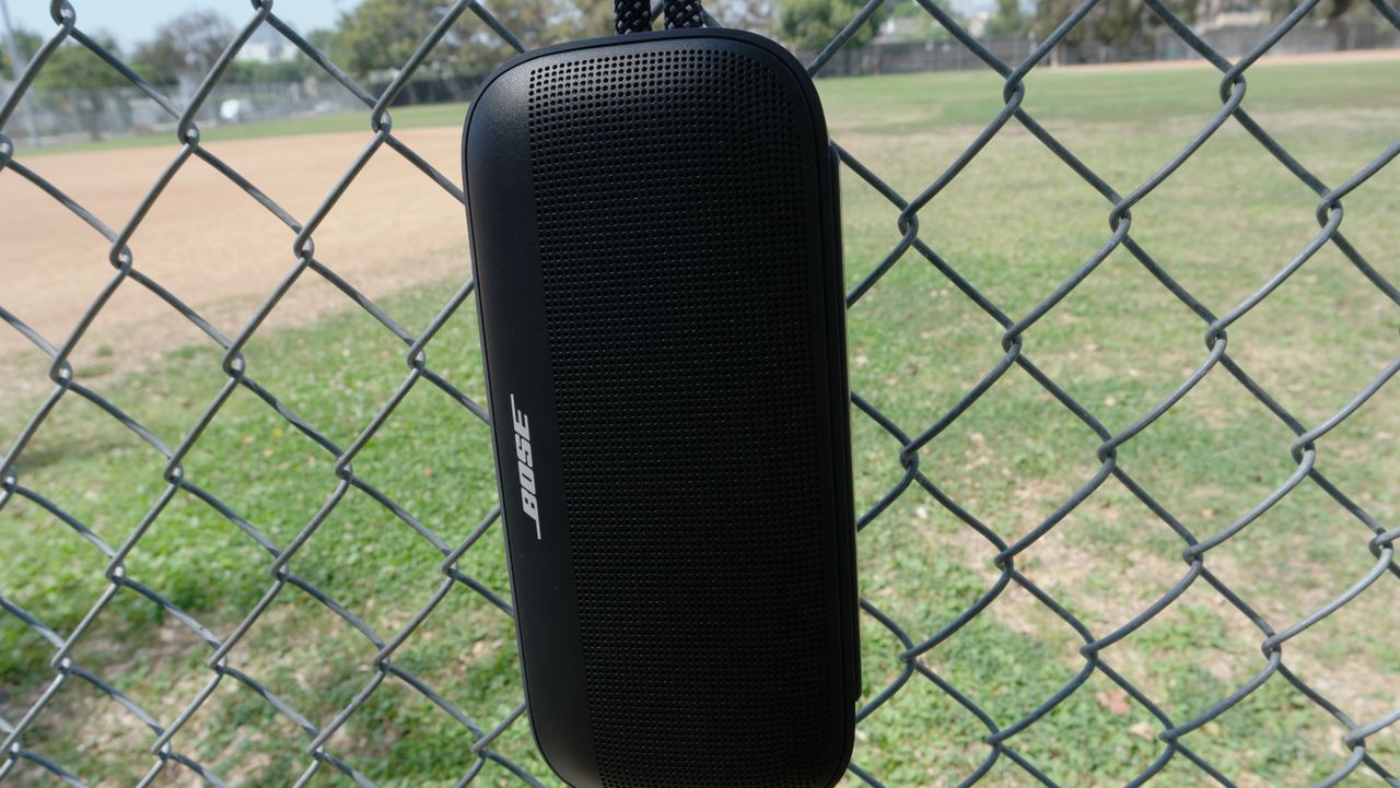 Bose SoundLink Plus hanging from a fence from the rugged nylon carry loop and a carabiner