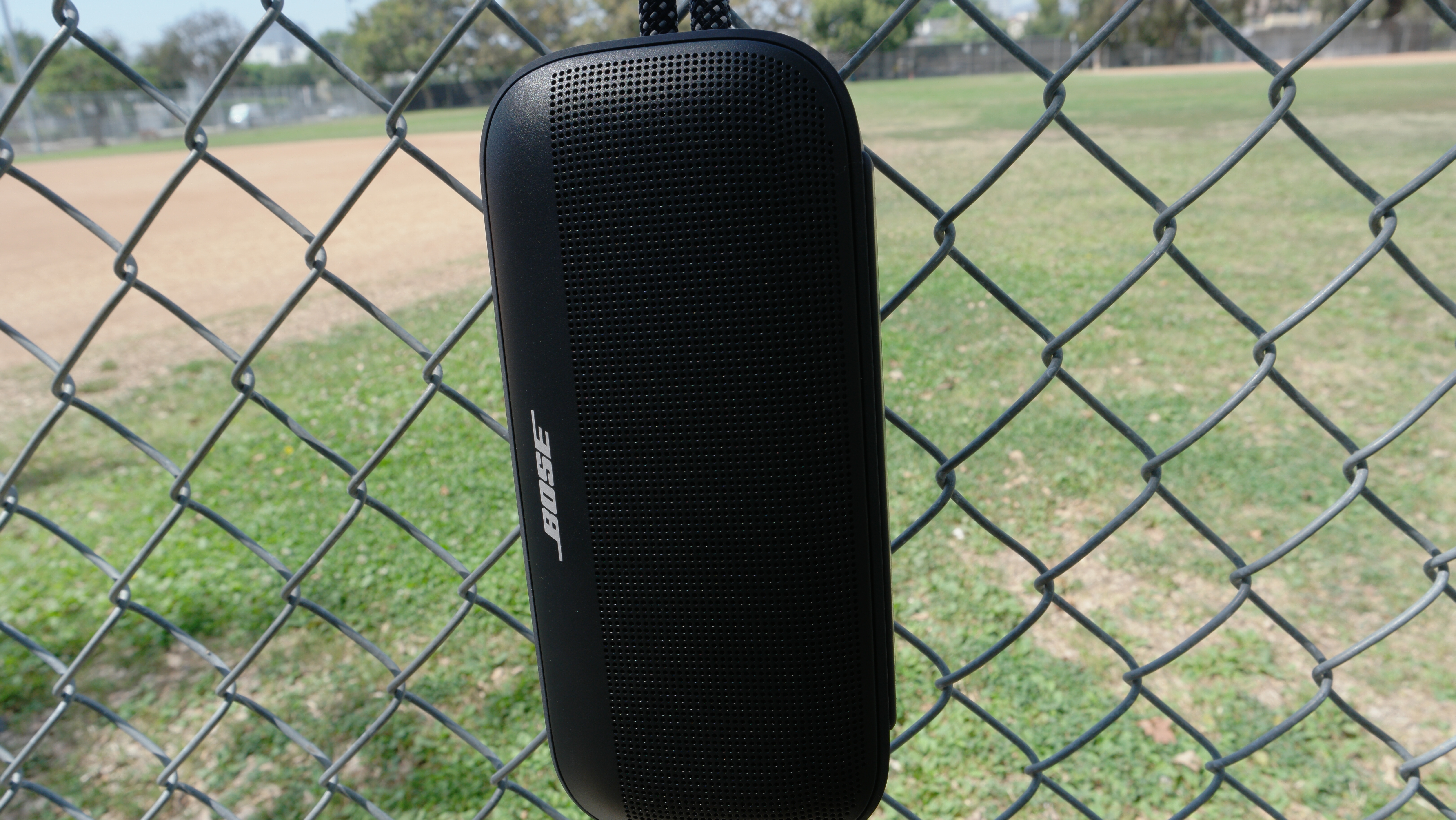 Bose SoundLink Plus hanging from a fence from the rugged nylon carry loop and a carabiner