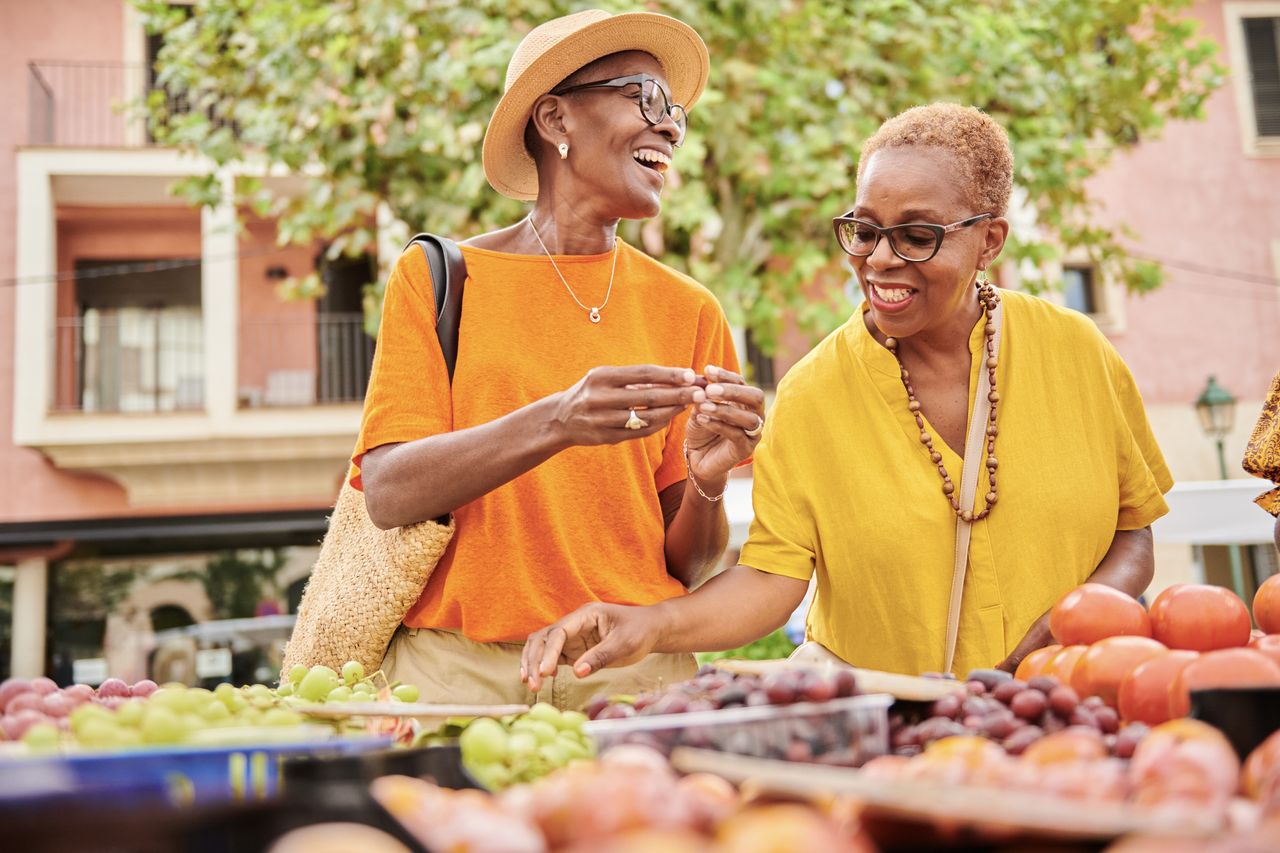 Two mature women shopping together at an outdoor food market.