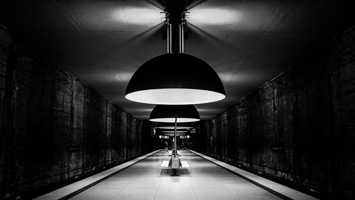 A black and white photo of a modern subway station with large hanging lamps