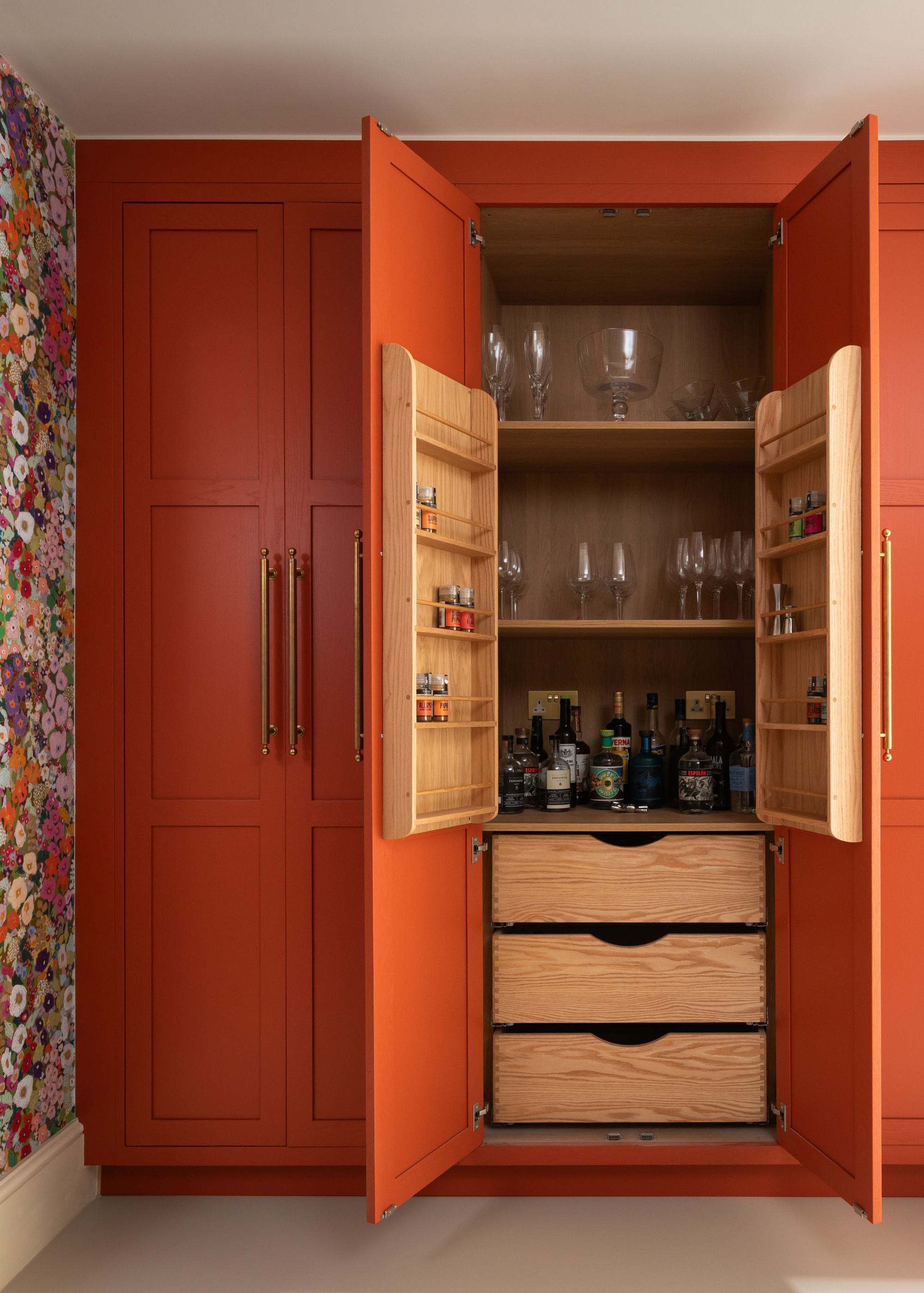 An orange hidden bar with double doors in a room with an accent wall of floral wallpaper