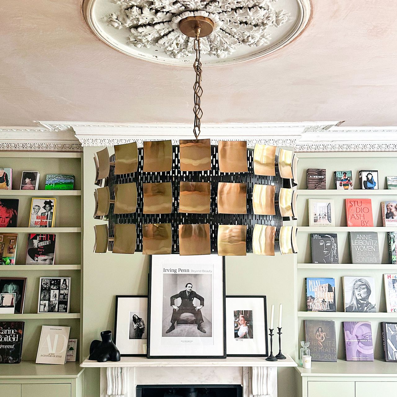 fireplace with pictures on the mantle and on shelves either side with a big chandelier