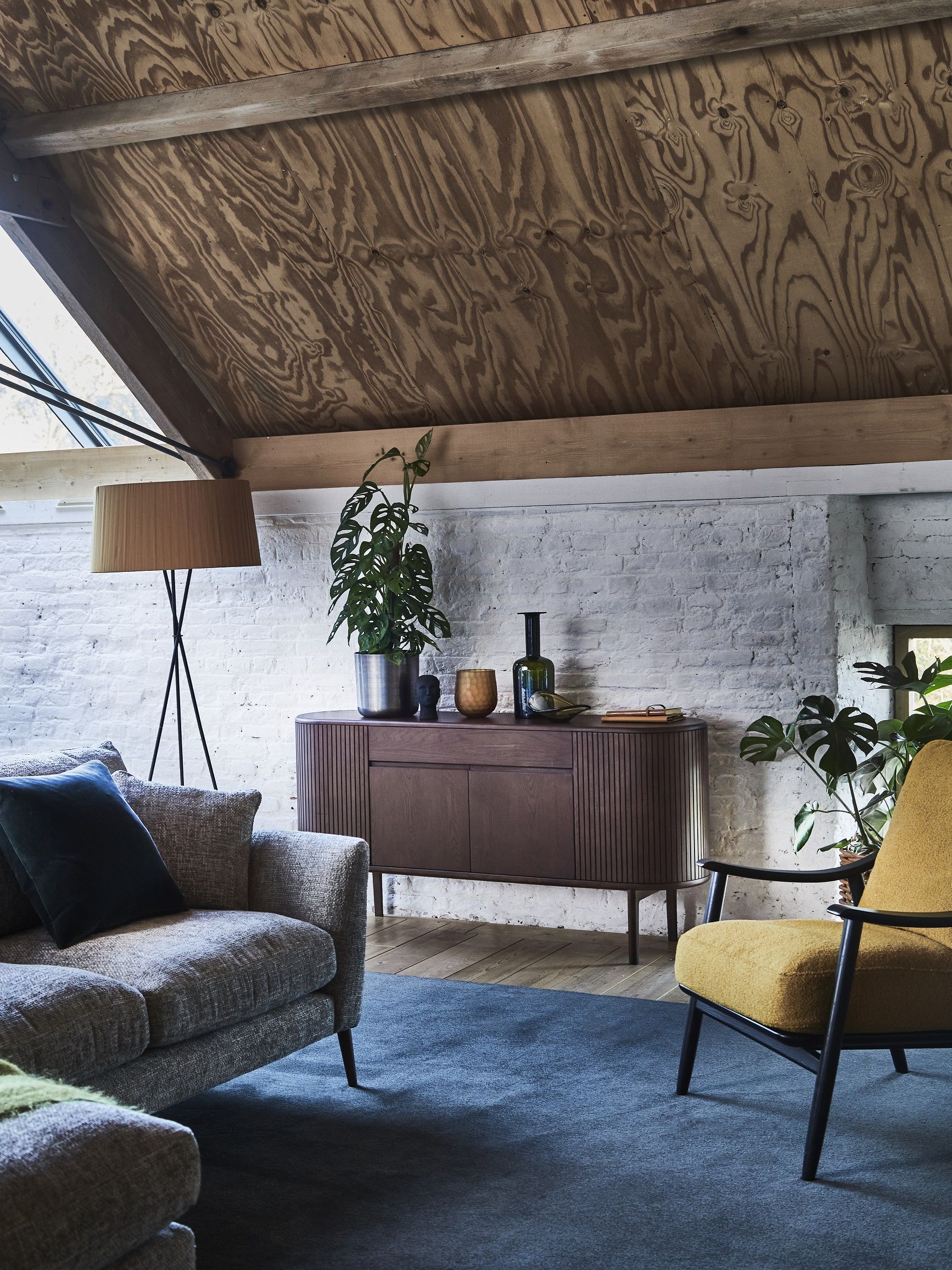 Living room with sofa and armchair, sideboard, wood floor and blue rug and white walls