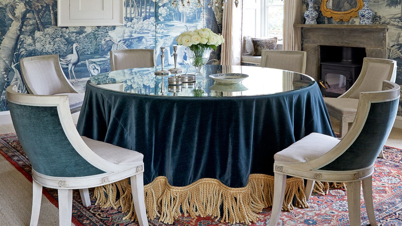 beamed blue dining room with scenic wallpaper fringed blue velvet tablecloth and Gustavian style dining chairs