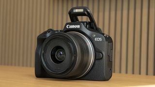 Canon EOS R100 camera on a table with built-in flash up