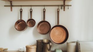 A copper pan set hanging on wall hooks above a kitchen counter