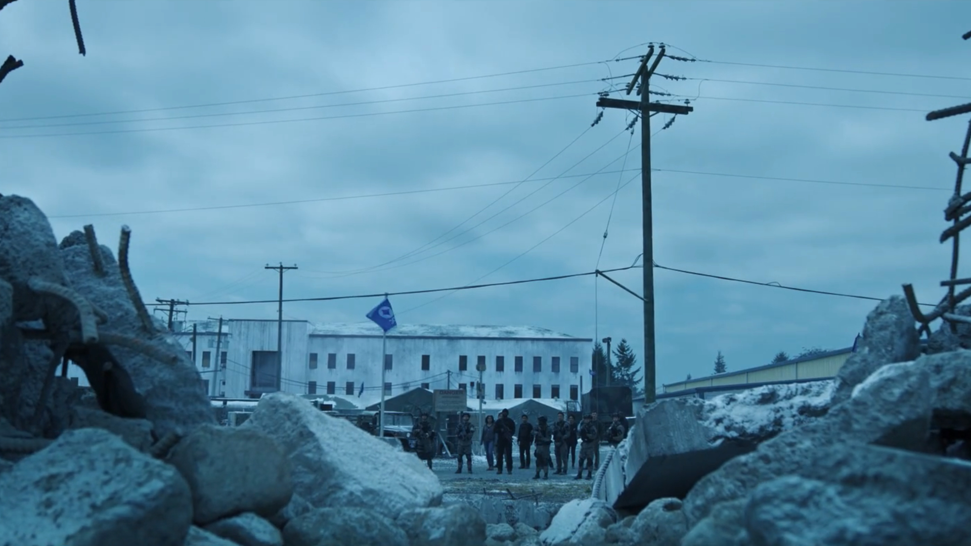 A group of civilians and soldiers look at a hole in a wall, surrounded by rubble