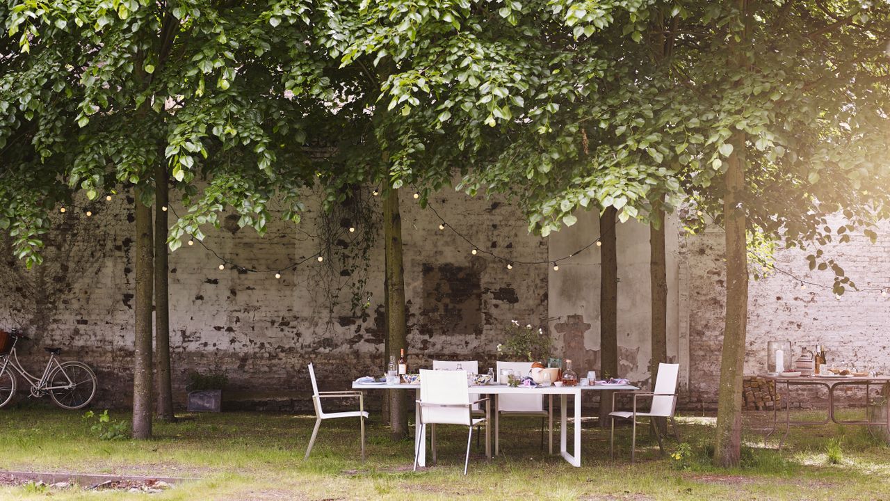 An outdoor dining area under a shaded tree covered spot with solar string lighting