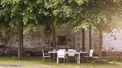 An outdoor dining area under a shaded tree covered spot with solar string lighting