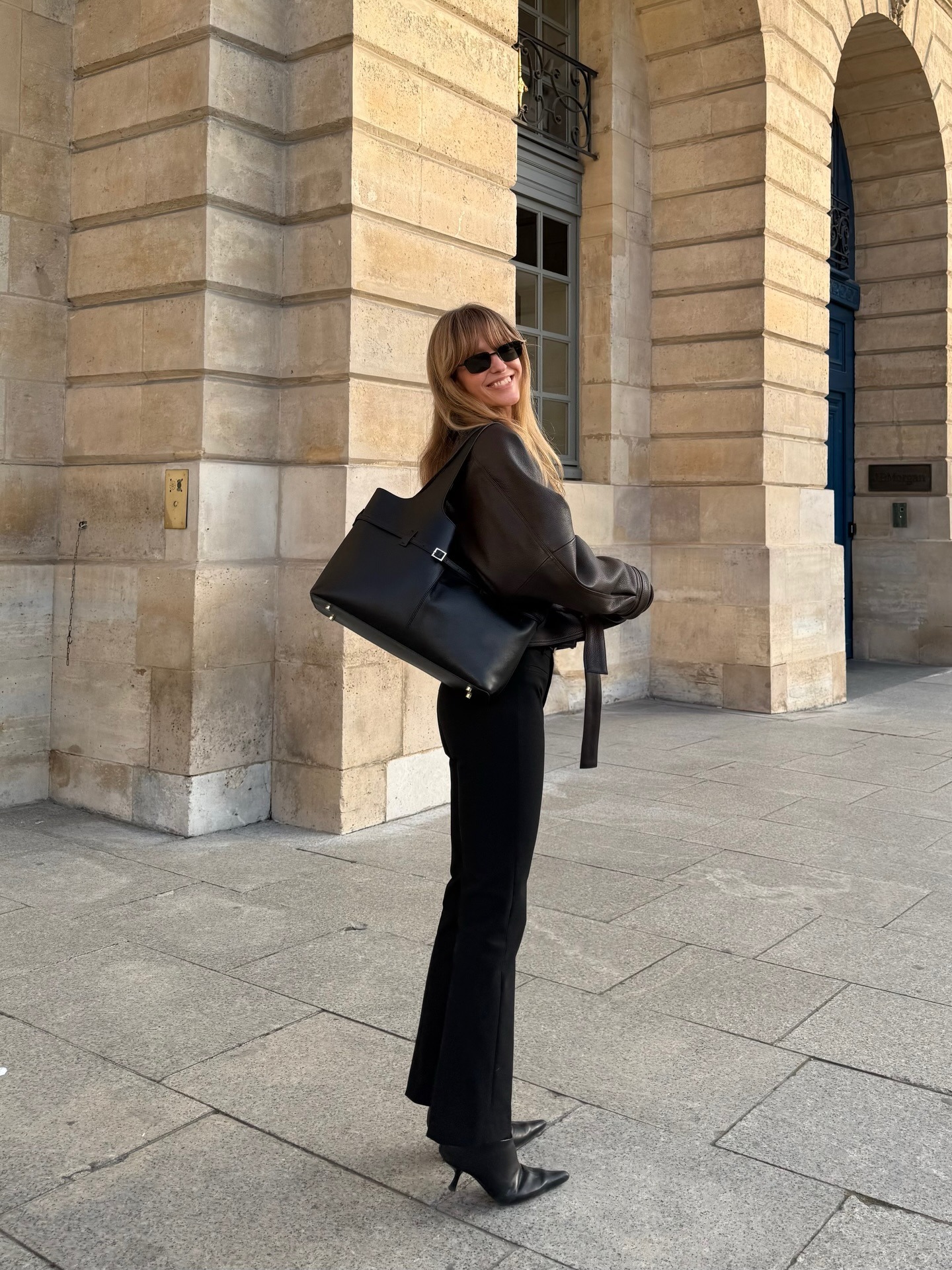 Woman wears black leather jacket, black jeans, caries black bag