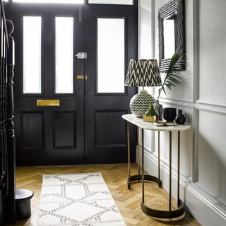 hallway with parquet floor and black door and marble console with lamp