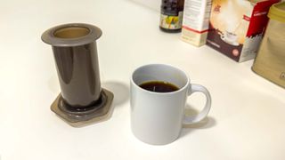 Aeropress coffee maker next to a coffee mug