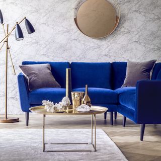 A small corner sofa with blue velvet upholstery in a living room with brass accessories