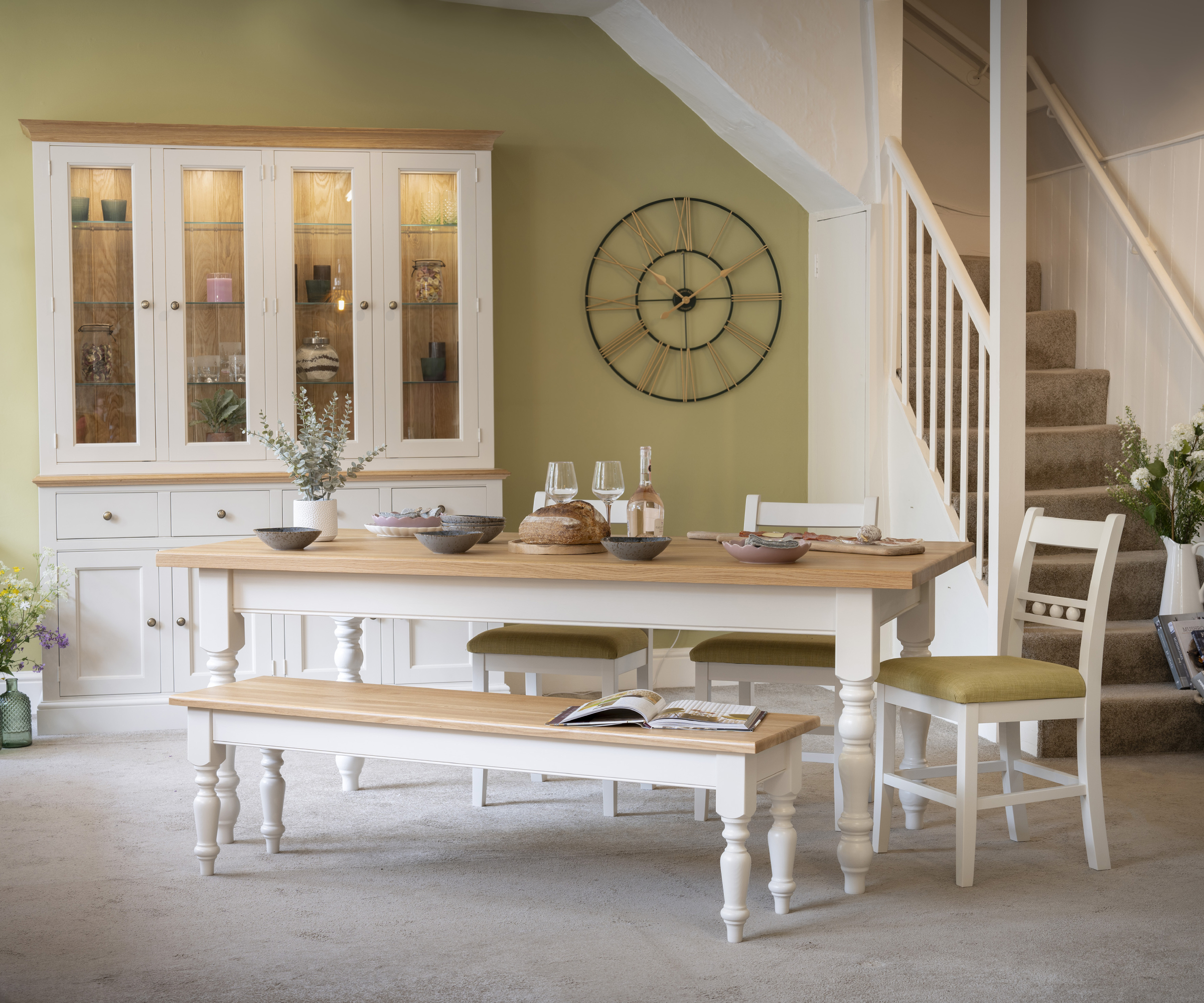 wood and white dining table with benches, storage cabinet and chairs in a room with green walls and staircase