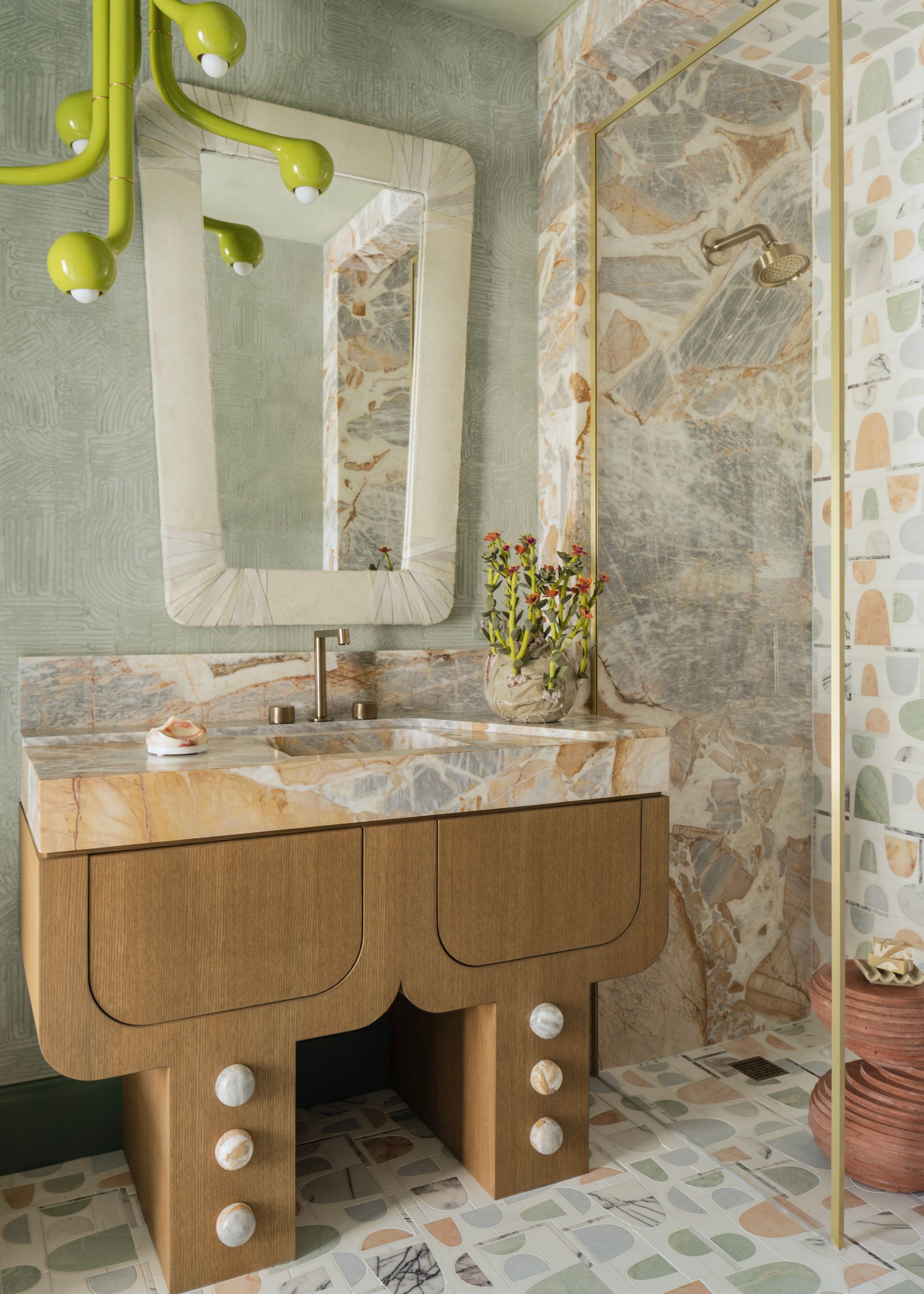A modern bathroom with a textured marble wall and matching sink countertop on a sculptural wooden unit. A fun, sage green and terracotta patterned tile on the floor and another wall in the shower.