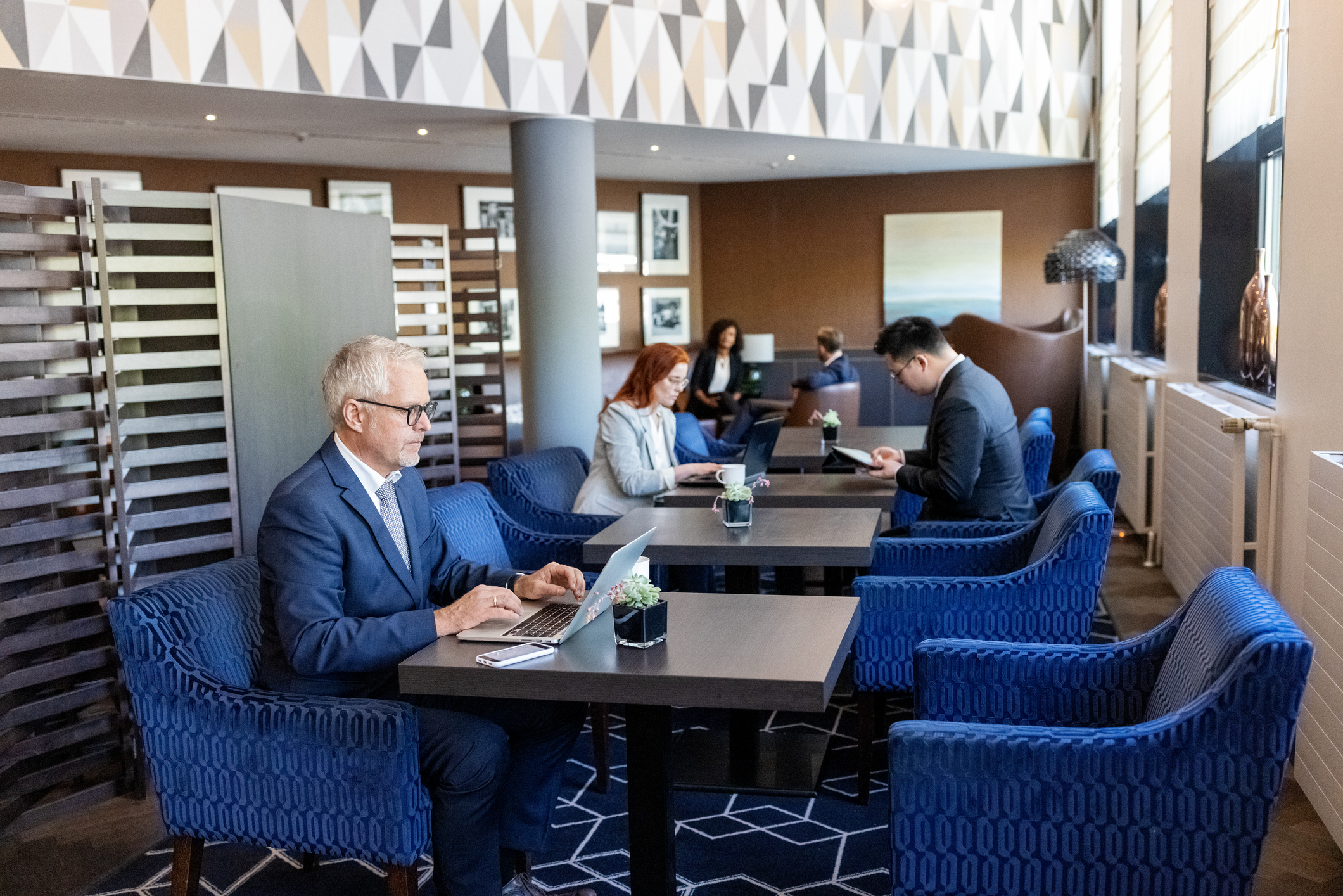 A senior business man works on his laptop while sitting inside an airport lounge.