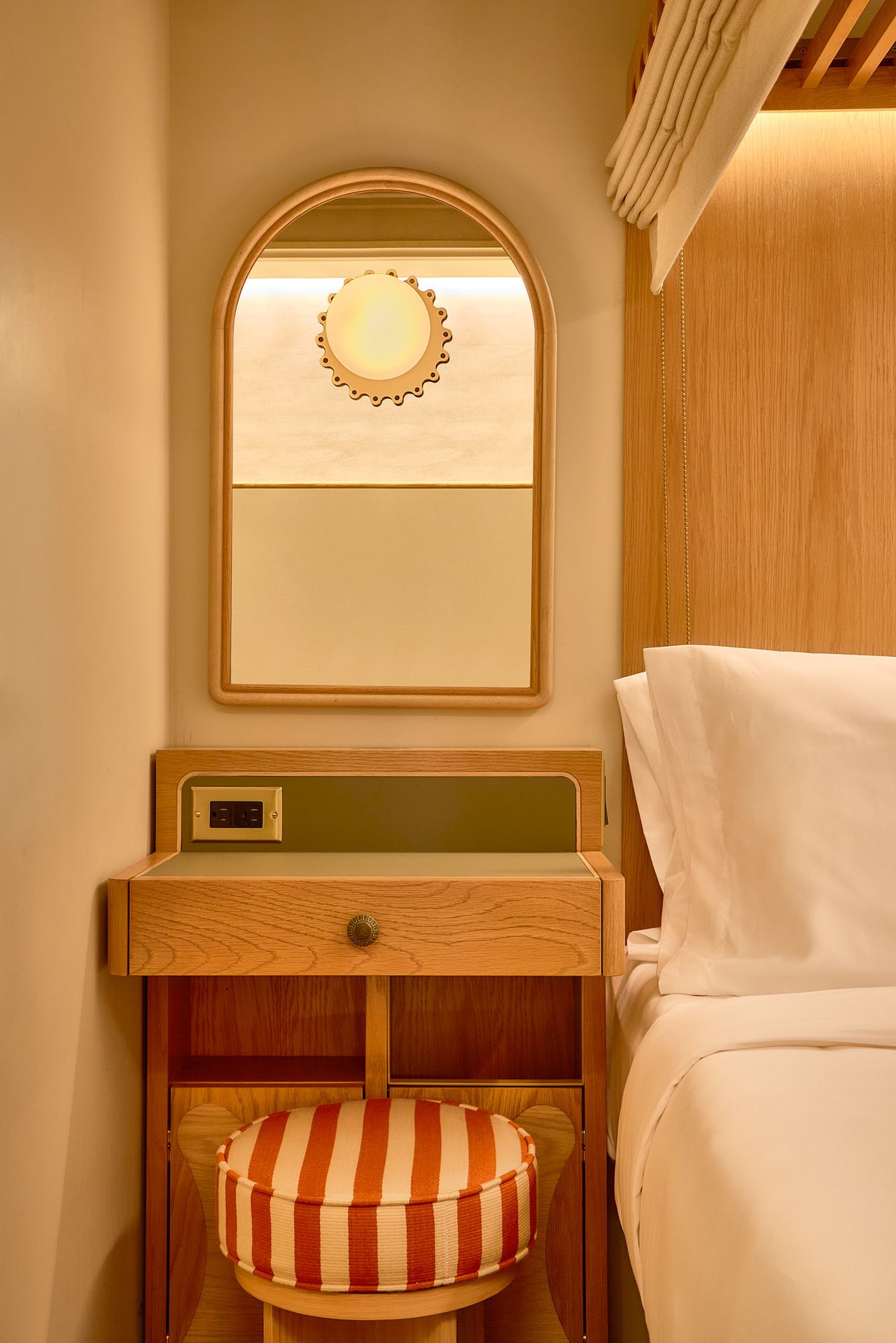 A sleeper train-inspired hotel features capsule-style rooms drenched in pale wood, stripy upholstery in red and cream, and Art Deco accents, including a tiled, purple-tinted shower and a murals-covered wall.
