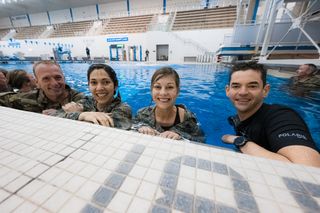 four astronauts in a pool. the camera view is close to the deck