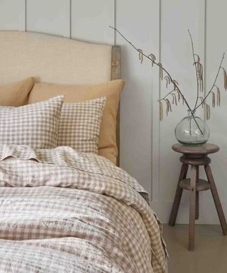 Mushroom Gingham Sheet Set on a bed against white walls beside a nightstand with a vase filled with feathers.