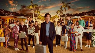 Against a tropical, palm tree-lined backdrop stands host Stephen Mangan and eleven duos of contestants, all clutching silver suitcases in a promotional photograph for The Fortune Hotel series 2.