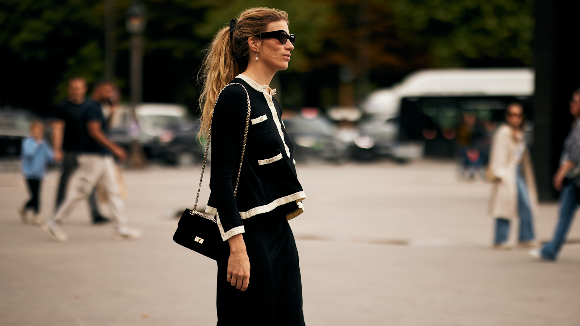 An attendee at Paris Fall Winter 2025, Haute Couture fashion week with a white and black sweater, sunglasses, and black crossbody bag