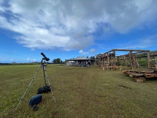 a camera on a tripod with a solar filter and a partly cloud sky above.