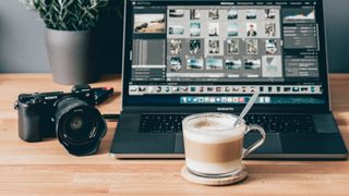 Laptop showing best photo-editing software next to a camera and coffee cup