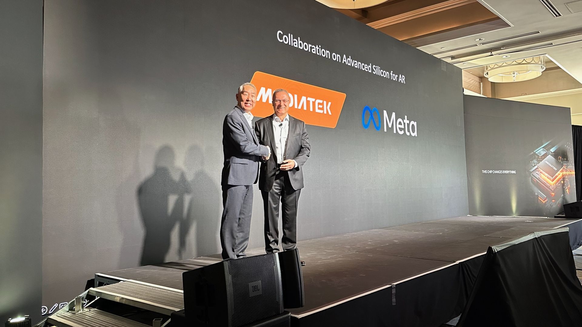 MediaTek VP Vincent Hu and Meta Reality Labs VP Jean Boufarhat shaking hands on stage at the MediaTek summit. The screen behind them announces their "collaboration on advanced silicon for AR."