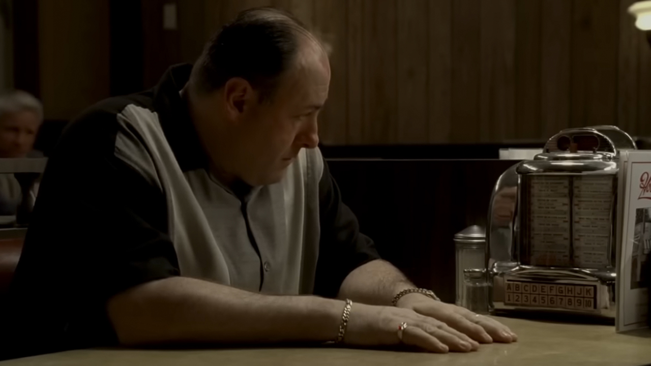 James Gandolfini sitting in a booth and looking at a jukebox in The Sopranos