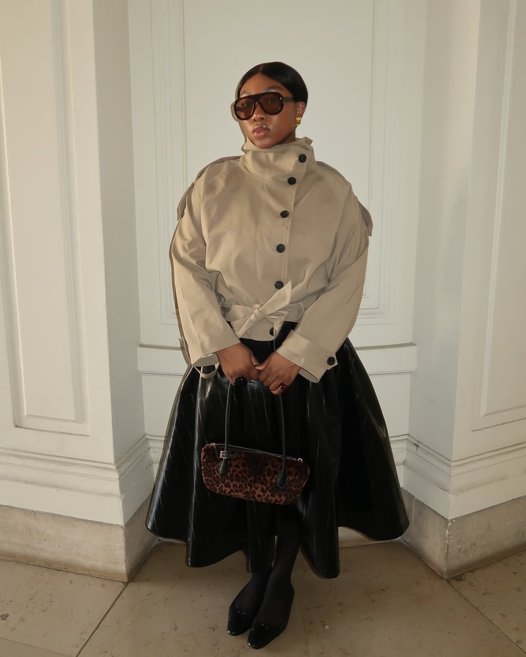 @nnennaechem wears a cropped trench, leather a-line midi skirt, ballet flats and a leopard bag
