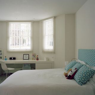 bedroom with white wall bed with designed cushion white window and white desk with chair