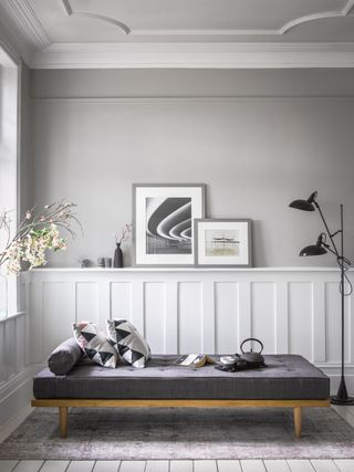 A grey living room with sofa bed, decorative ceiling coving, framed wall art, and a black floor lamp