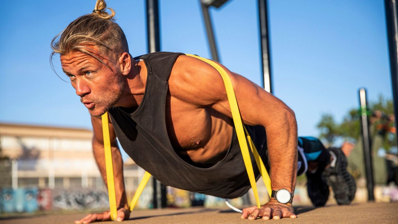 A man performing a resistance band push-up as part of a full-body strength training workout 