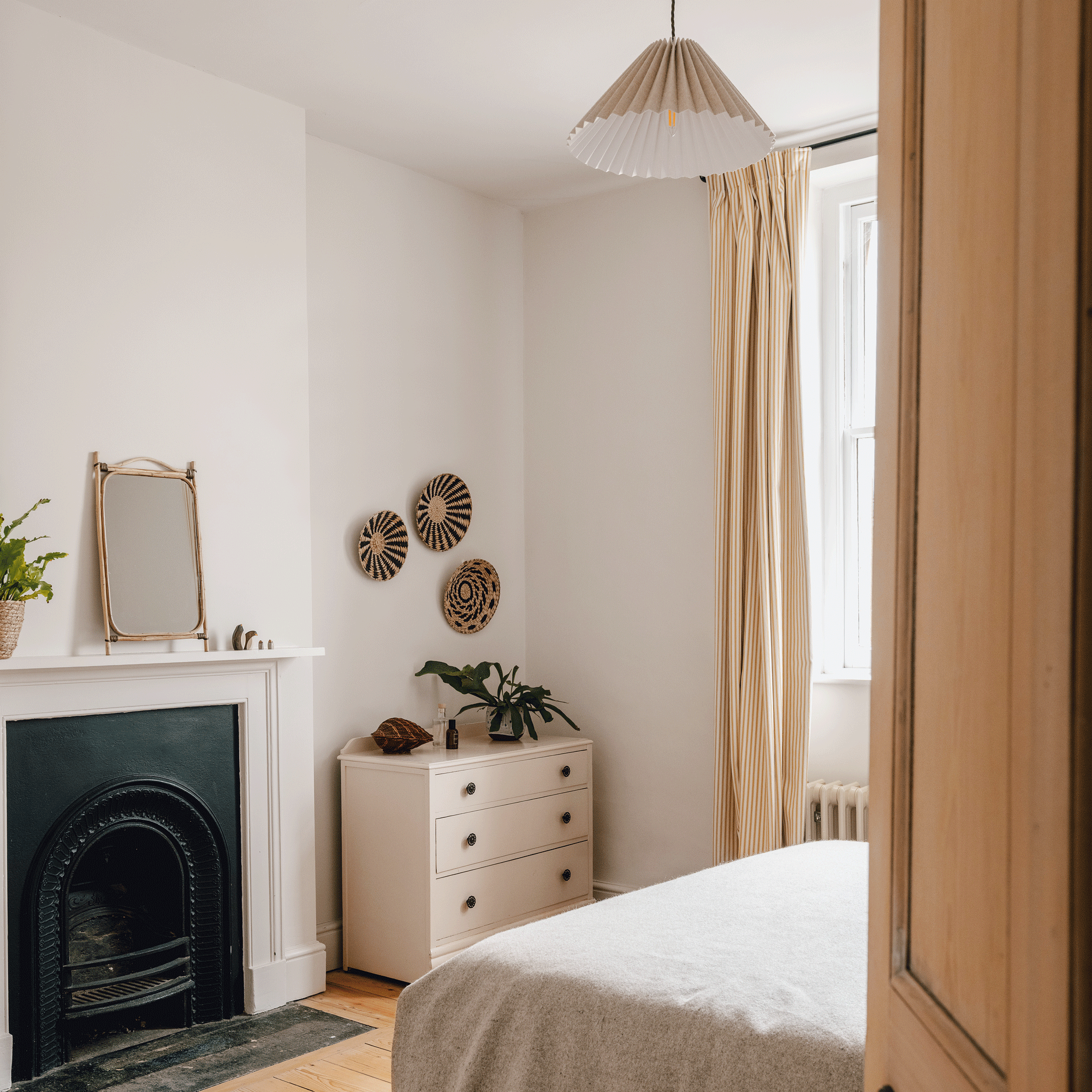 a neutral bedroom with a chest oof drawers and traditional cast iron fronted fireplace